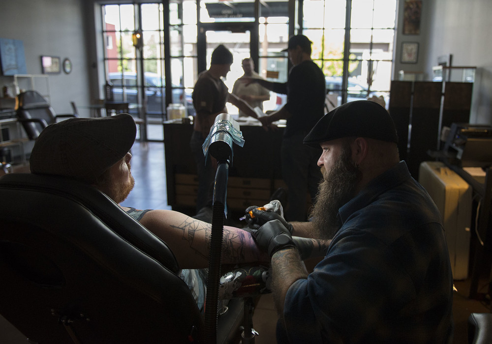 A lamp illuminates customer Joel Schmid of Camas, left, as he chats with tattoo artist Ryan "Boomer" Boomhower while getting a tattoo with a Columbia River Gorge theme at 3rd Heart Tattoo on Tuesday afternoon, Oct. 6, 2015 in Washougal. (Amanda Cowan/The Columbian)