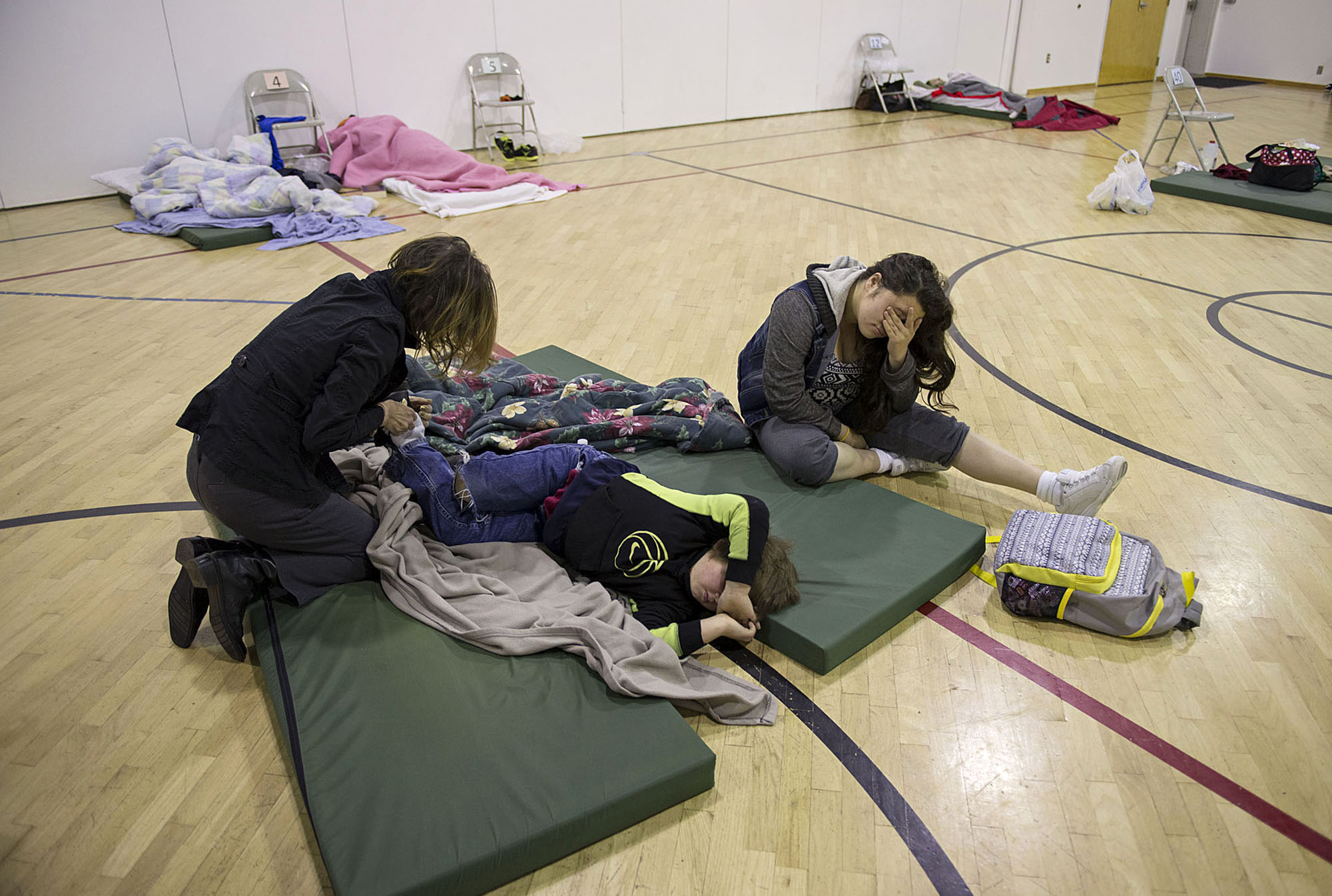 Donna Pinaula, from left, helps get her kids Johnny Pinaula, 7, and Shyanne Tanguileg, 16, ready as they slowly wake up at 6:45 a.m. after sleeping on the floor of the St. Andrew Lutheran Church gym Tuesday morning, Nov. 17, 2015 in Vancouver. The Winter Hospitality Overflow shelter provides a warm place to stay to those in need during winter's coldest months. (Amanda Cowan/The Columbian)