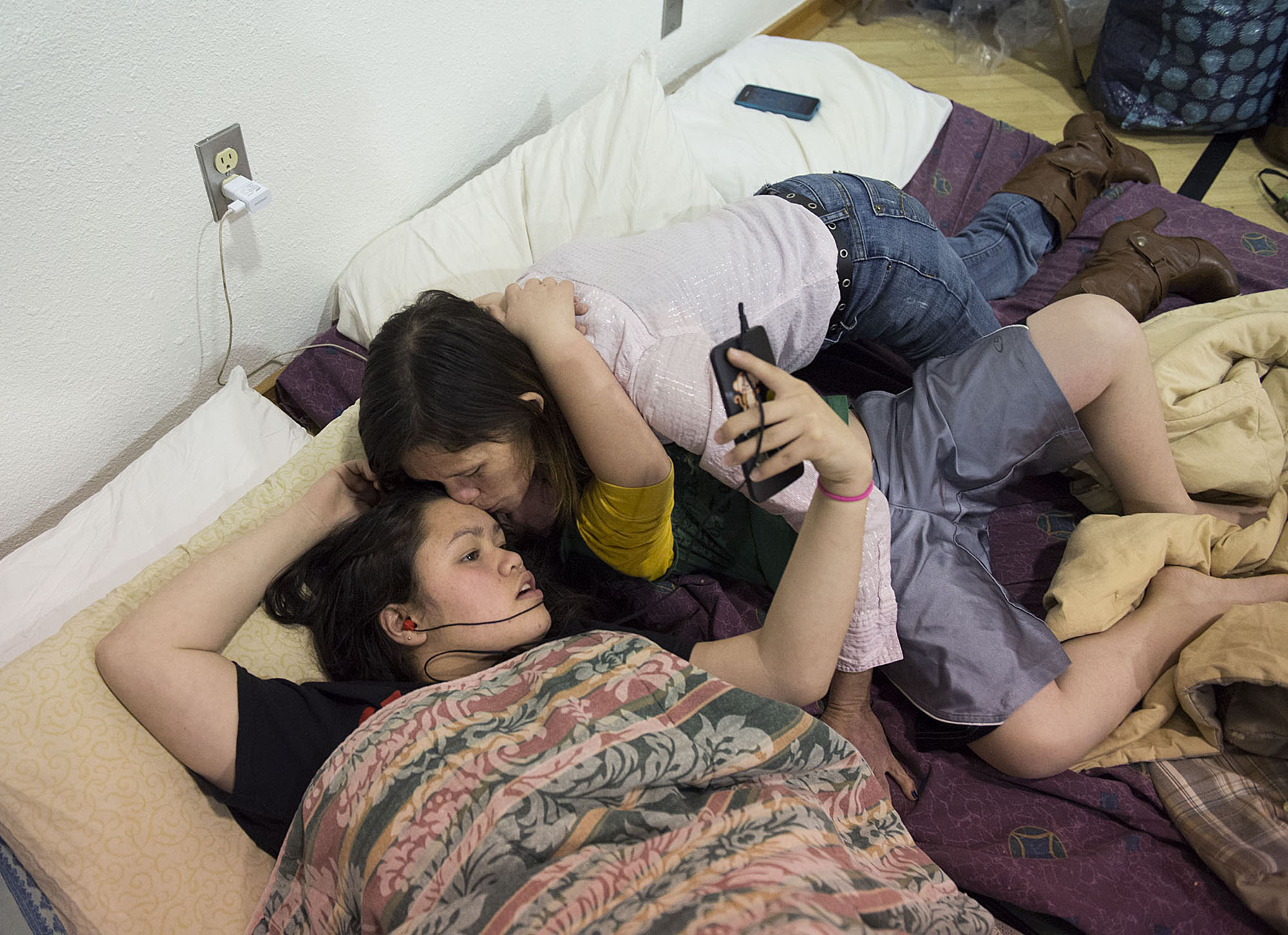 Shyanne Tanguileg, 16, left, gets a kiss from her mom, Donna, right, as they settle in for the night with her brother, Johnny Pinaula, 7, in gray shorts, Wednesday night, Dec. 2, 2015 at the Winter Hospitality Overflow at St. Andrew Lutheran Church. (Amanda Cowan/The Columbian)
